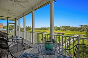 A covered outdoor area with a table and chairs, a decorative vase, and a view of a green landscape. - Ale Of A Good Time: Modern Home Overlooking Canal (Oak Island)