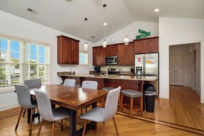 A modern kitchen with wooden cabinets, a large island, and a dining area with a wooden table and grey chairs. - Ale Of A Good Time: Modern Home Overlooking Canal (Oak Island)