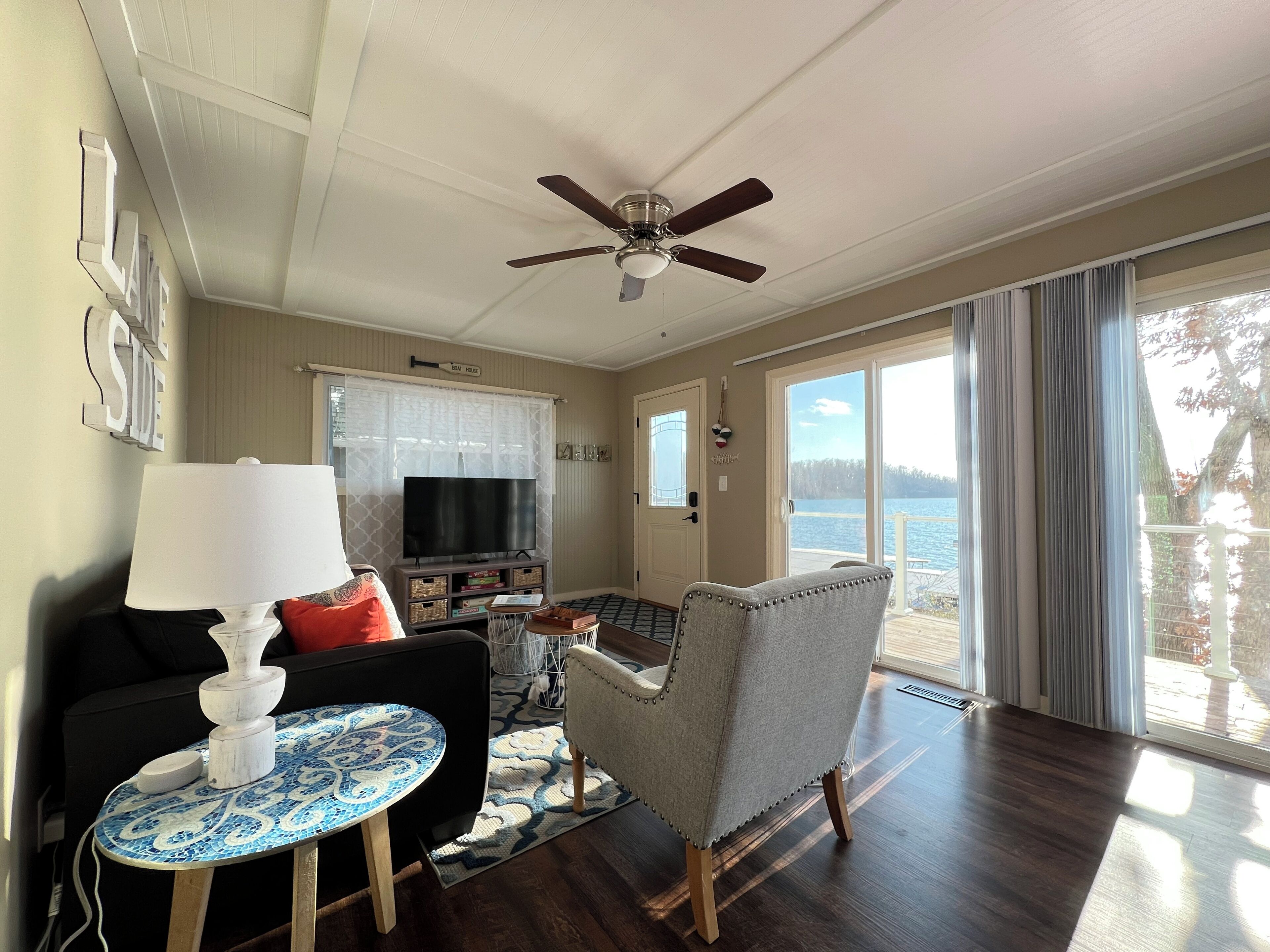 A living room with a ceiling fan, a TV, a sofa, a chair, and a view of the outdoors.