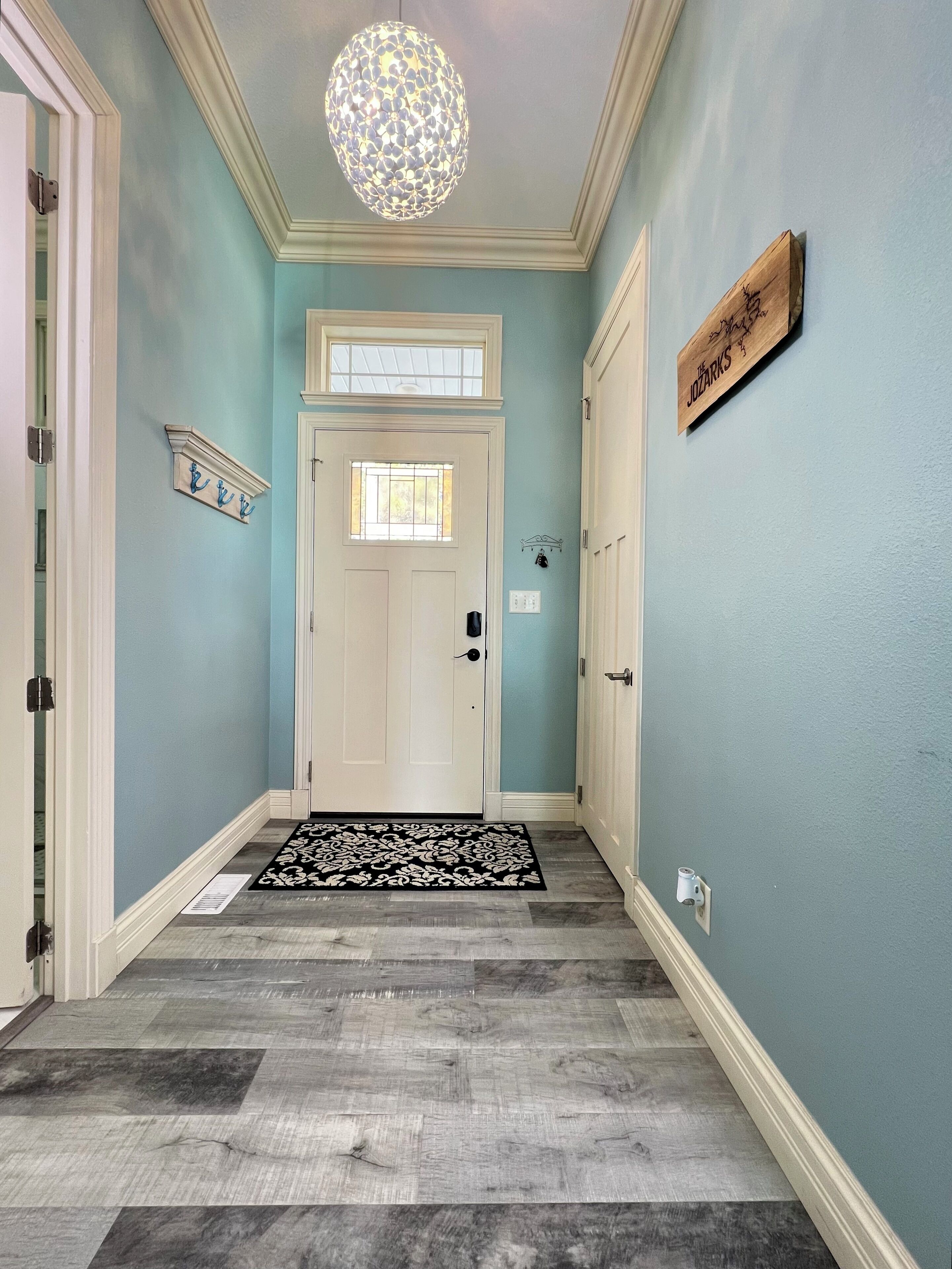 A hallway with a white door, a decorative ceiling light, a nameplate, and a patterned rug.