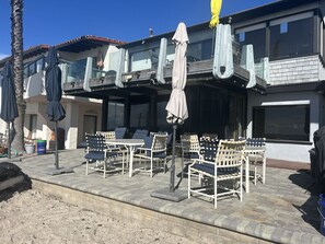 An outdoor seating area with tables and chairs, umbrellas, and a building with balconies. - Whale Rock House Beach Front (2nd FL) - (STR#03-2662) (Dana Point)