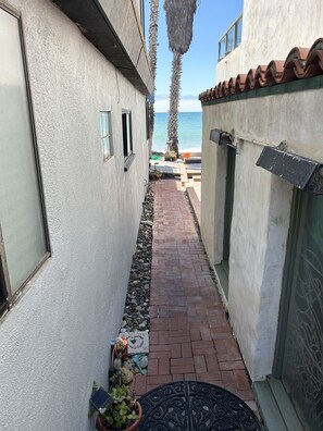 A narrow pathway flanked by buildings with a view of the sea.