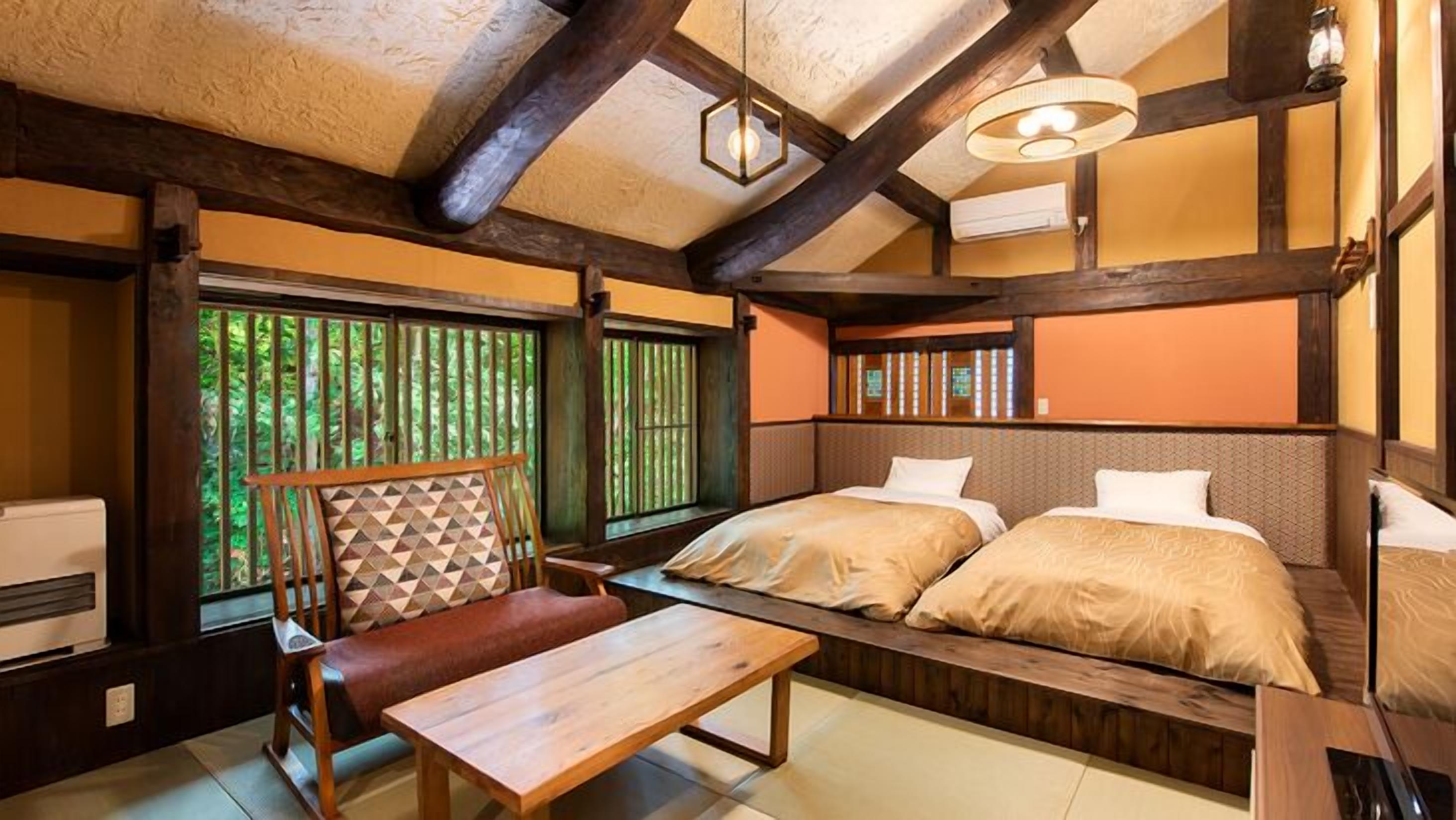 Ein traditioneller japanischer Raum mit Tatami-Boden, einem niedrigen Holztisch, einer gepolsterten Bank und einem Bett mit einem Holz-Kopfteil.