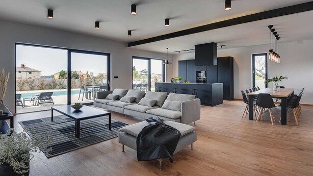 A modern living room with a grey sofa, a dining area with a wooden table, and a kitchen with dark cabinets. - Villa Polei with Pool (Pula)