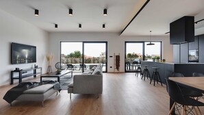 A modern living room with a grey sofa, a coffee table, and a TV displaying a stormy cityscape. - Villa Polei with Pool (Pula)