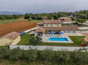 Une grande maison avec une piscine, un espace salon extérieur et une vue sur la campagne.