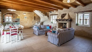 A spacious living area with a high wooden ceiling, a fireplace, striped sofas, and a dining area with white chairs and a table set for a meal. - Holiday Home Tranquil with Pool (Krnica)