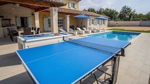 A pool table and a pool in a backyard with outdoor seating and a building in the background. - Holiday Home Tranquil with Pool (Krnica)