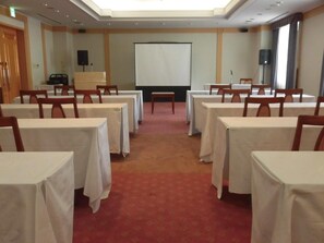 A conference room with tables and chairs, a projector screen, and a carpeted floor. - Business Hotel Noda (Noda)