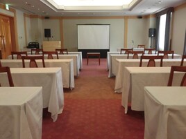 Un salón de conferencias con mesas, sillas, una pantalla de proyector y piso alfombrado.