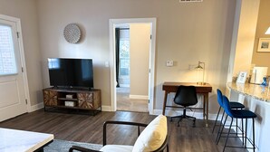 Ett modernt vardagsrum med en platt-TV, ett matbord, en soffa och en köksdel med barstolar.