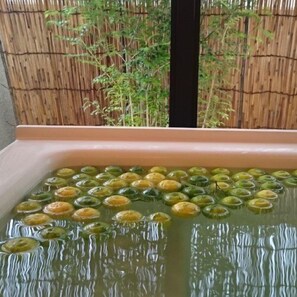 Una fuente rectangular con varios objetos redondos flotando en su interior, con un cerco de bambú de fondo.