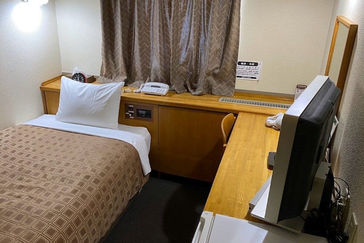 Habitación de hotel con cama, escritorio con teléfono y computadora, espejo y un cartel en la pared.