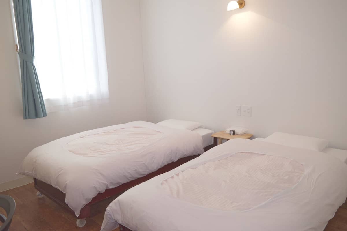 A room with two single beds, a small bedside table with a lamp, and a window with curtains.