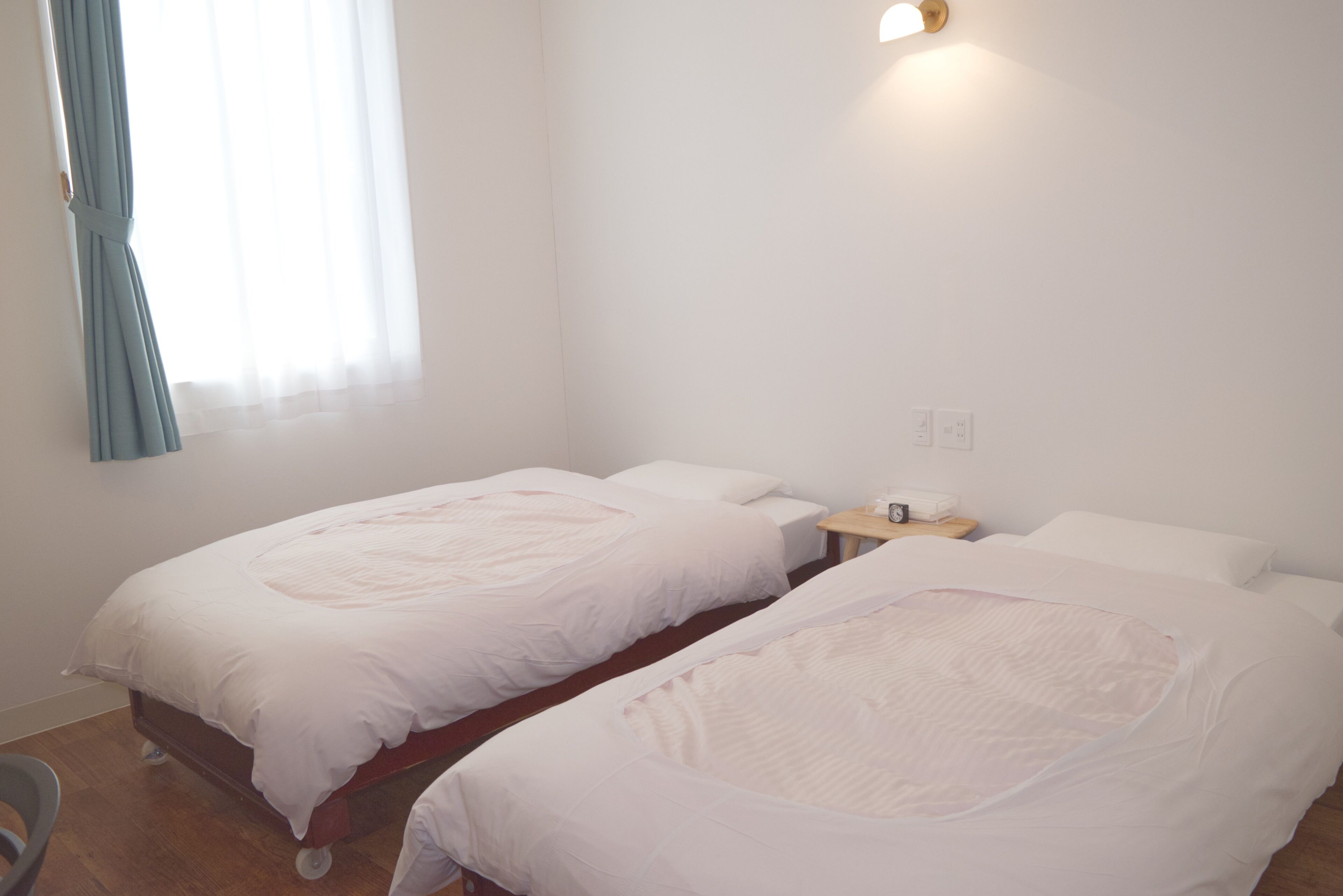 A room with two single beds, a small bedside table, a chair, and a window with curtains.
