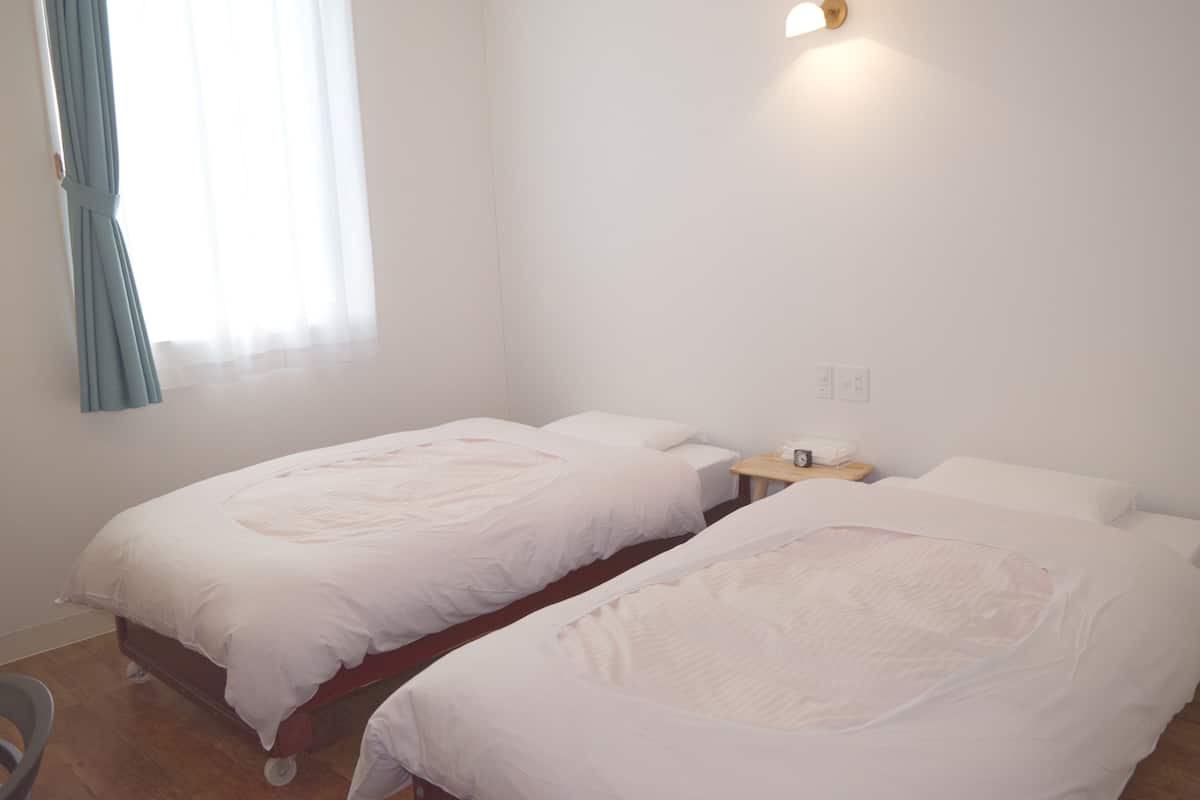 A room with two single beds, a small bedside table, a chair, and a window with curtains.