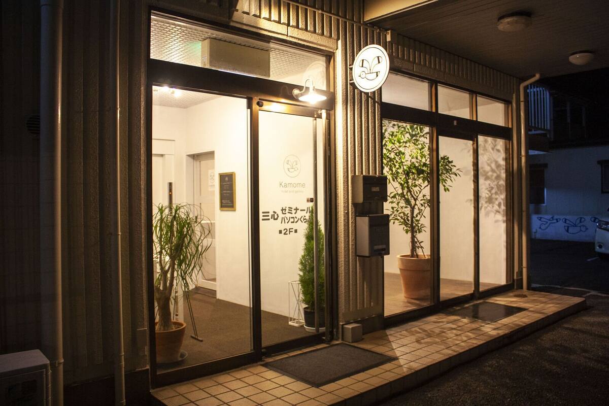 A building with a glass entrance, a sign with Japanese characters, and a potted plant outside.