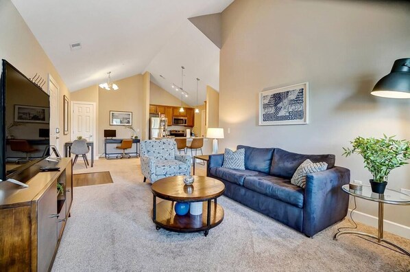 A spacious living room with a dark blue sofa, a round coffee table, and a dining area in the background.
