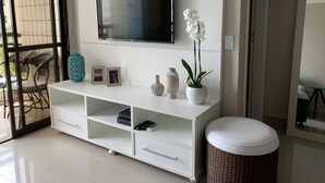 Una sala de estar moderna con un mueble blanco para entretenimiento, un televisor de pantalla plana, jarrones decorativos y una planta de orquídea.