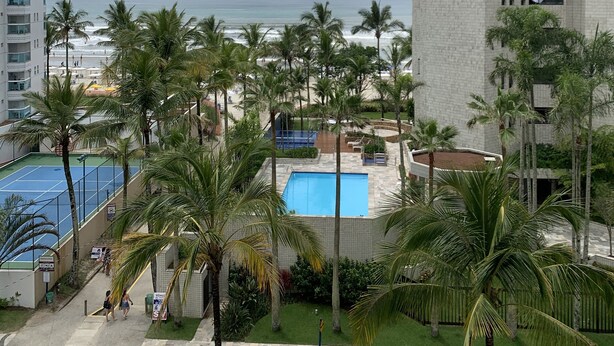 Vista de un hotel con piscina, palmeras y una playa al fondo.