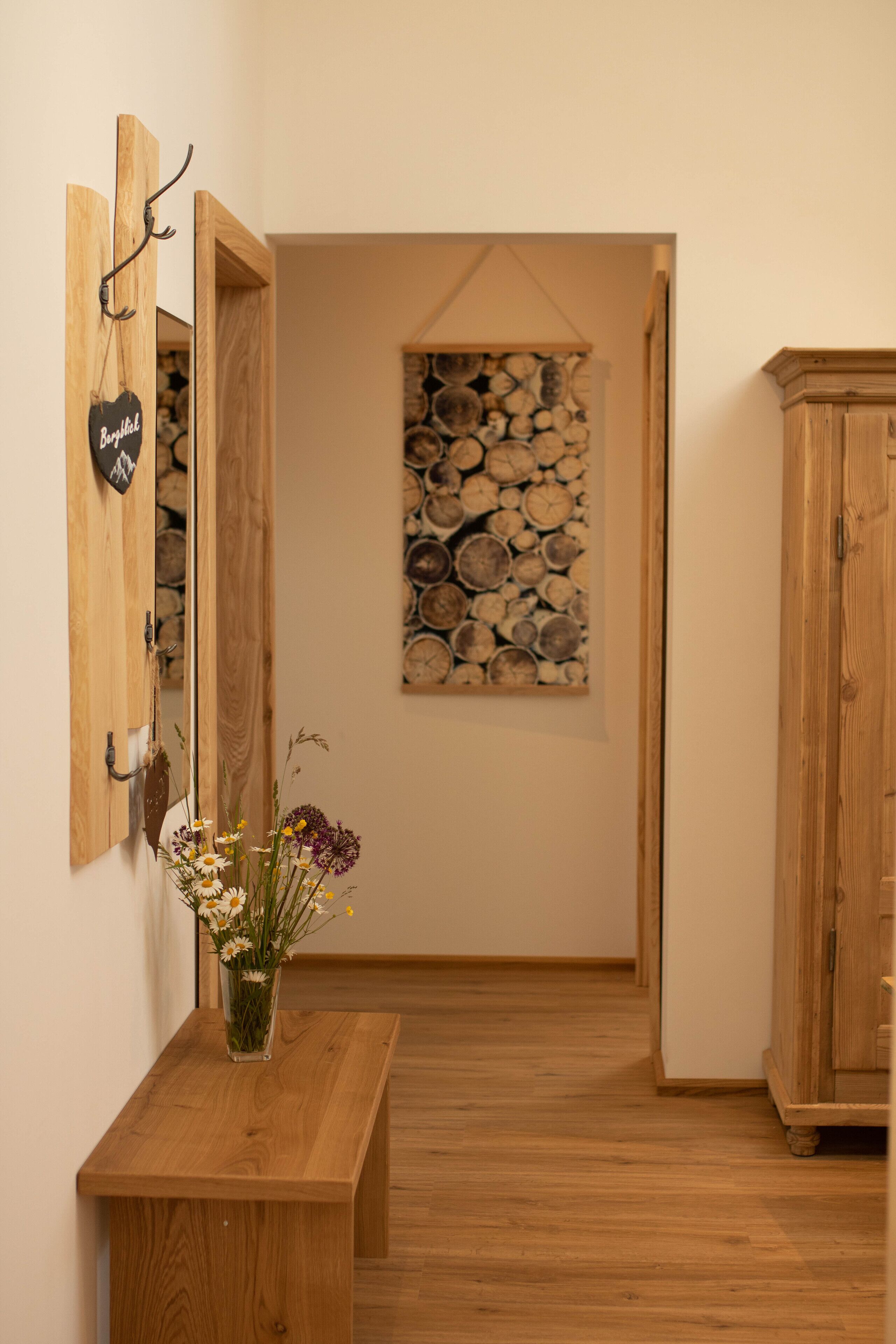 Een houten bank met een bloemenvaas, een wandkapstok en een decoratie van hout in een gang.