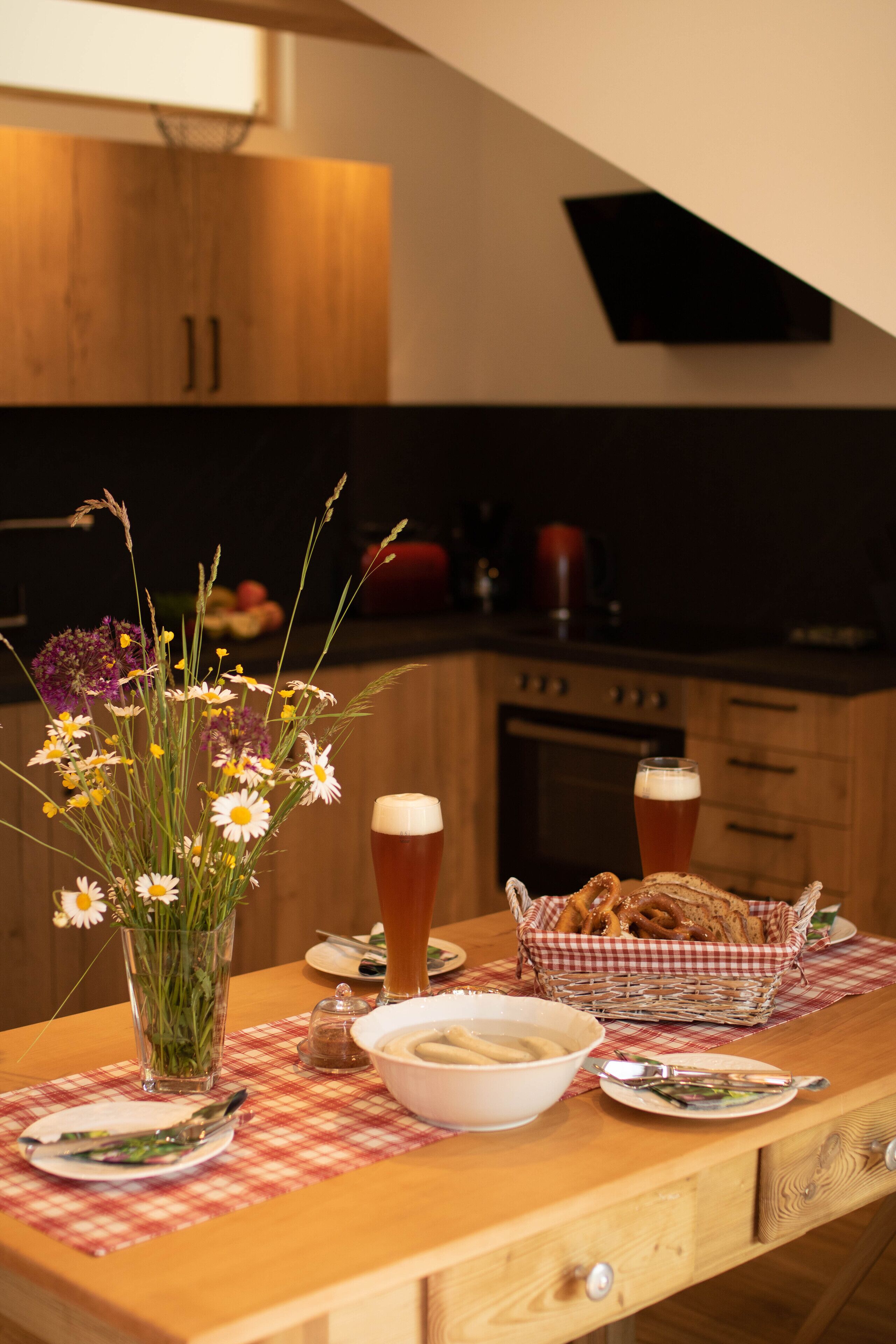 Une table à manger ornée d’un vase de fleurs, d’un panier de pain et de deux verres de bière.
