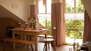 A cozy dining area with a wooden table, benches, and a view of greenery through large windows.