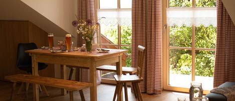 A cozy dining area with a wooden table, benches, and a view of greenery through large windows.