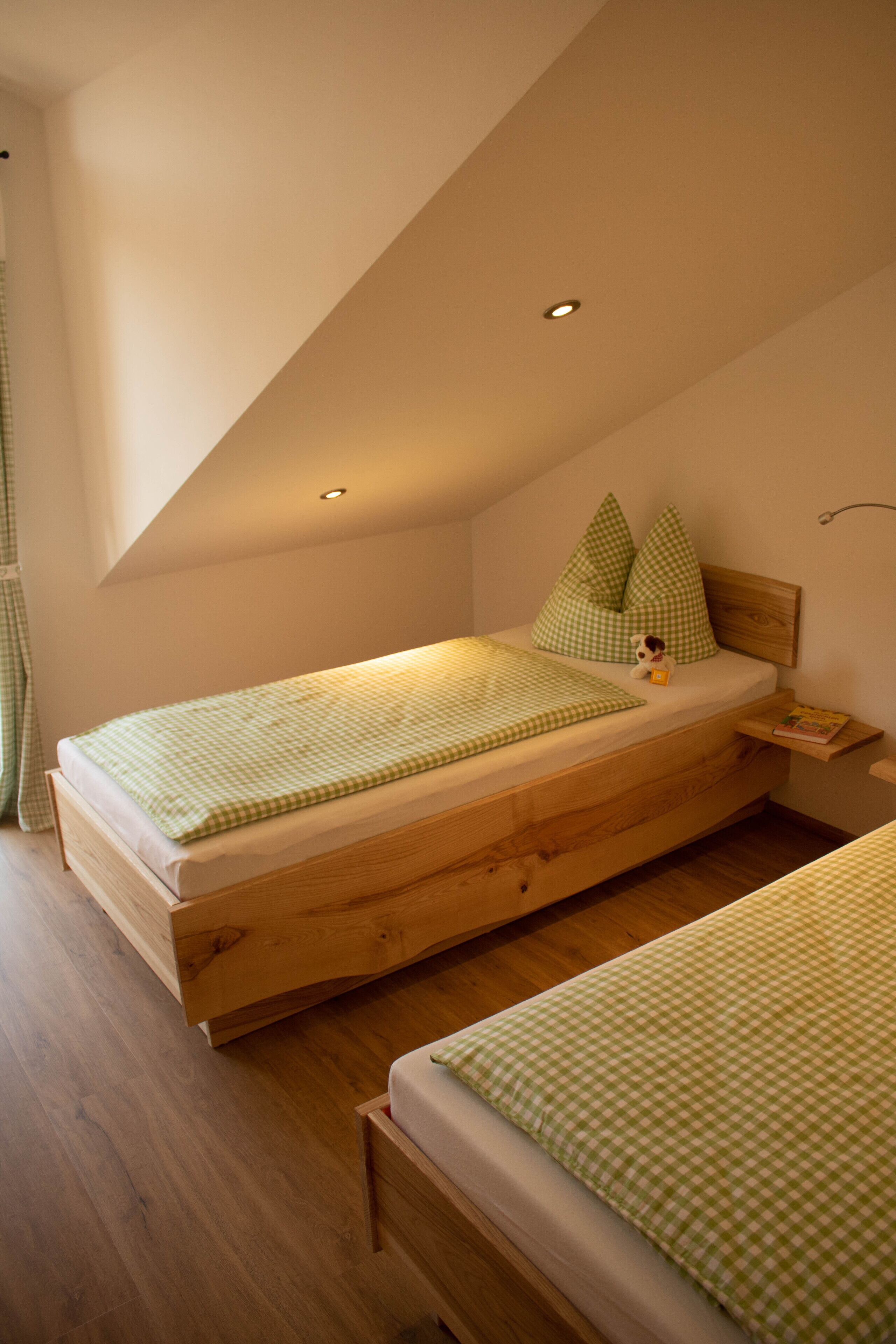 A small, cozy bedroom with a sloped ceiling, a wooden bed, and a nightstand.