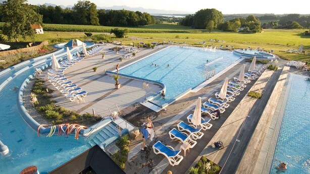 A large outdoor swimming pool with multiple lanes, surrounded by lounge chairs and umbrellas.