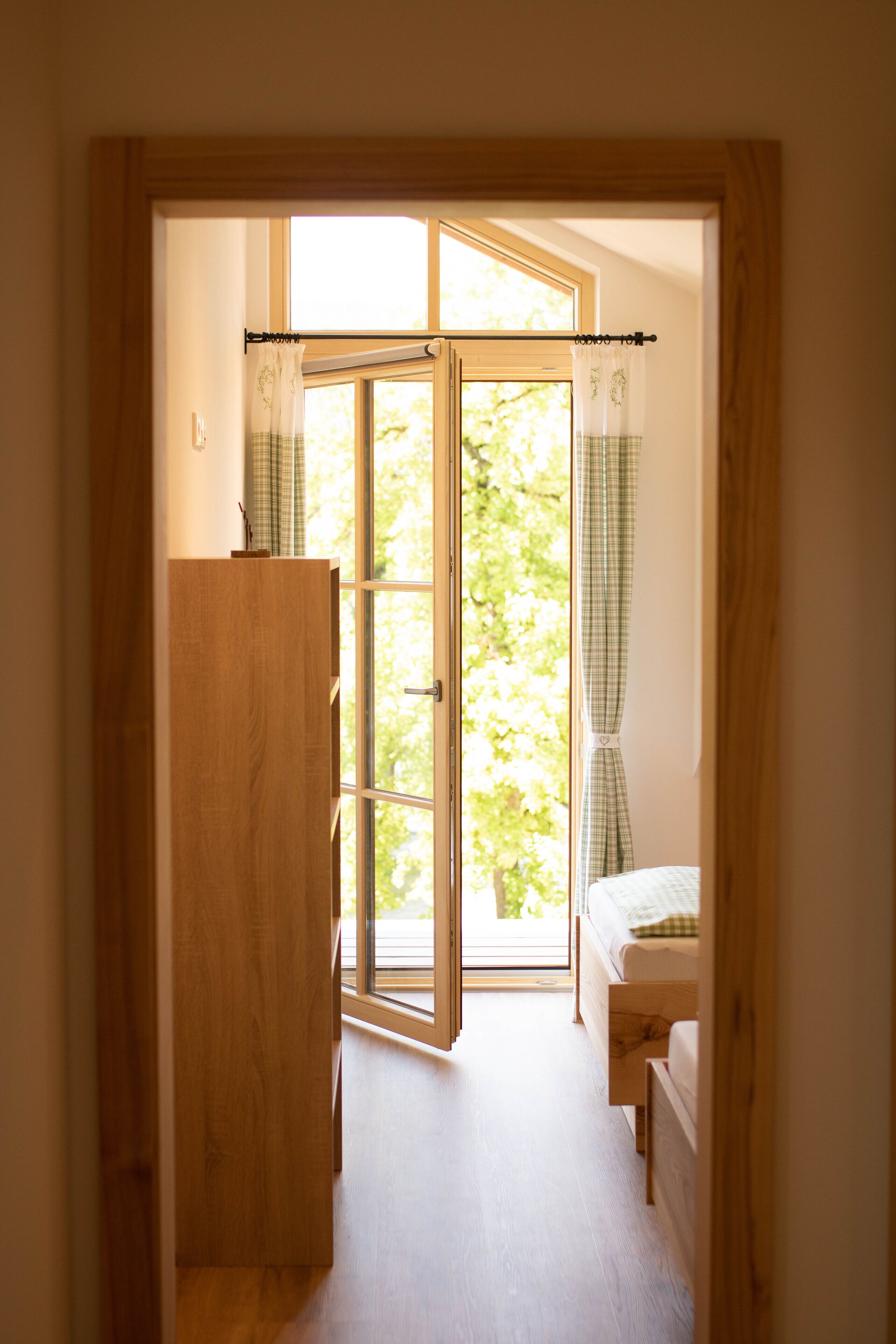 A bedroom with a wooden wardrobe, a bed with a checkered bedspread, and a window with curtains.