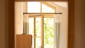 A bedroom with a wooden wardrobe, a bed with a checkered bedspread, and a window with curtains.