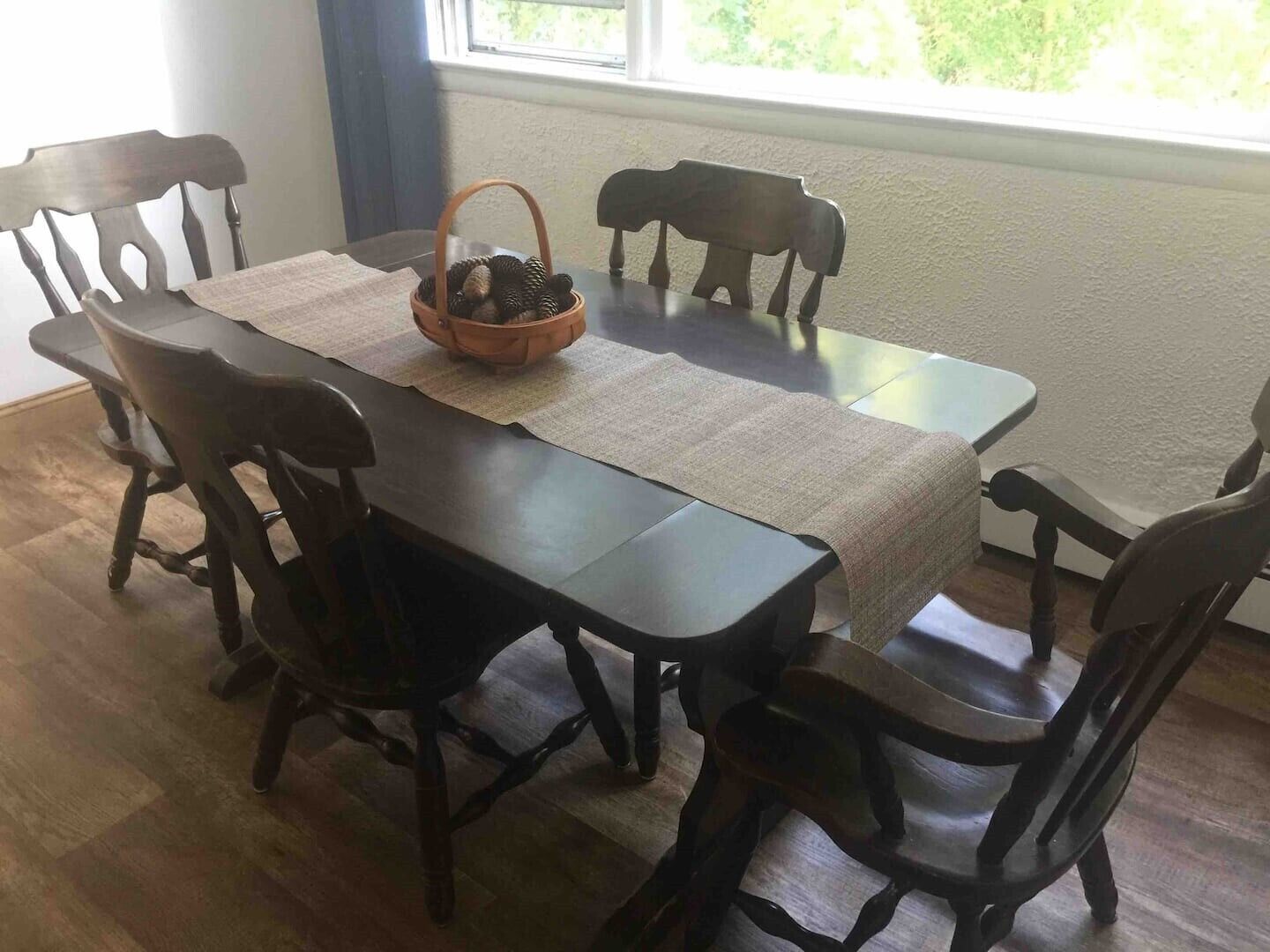 Une table à manger surmontée d’un set de table en fibres tressées, entourée de chaises en bois.