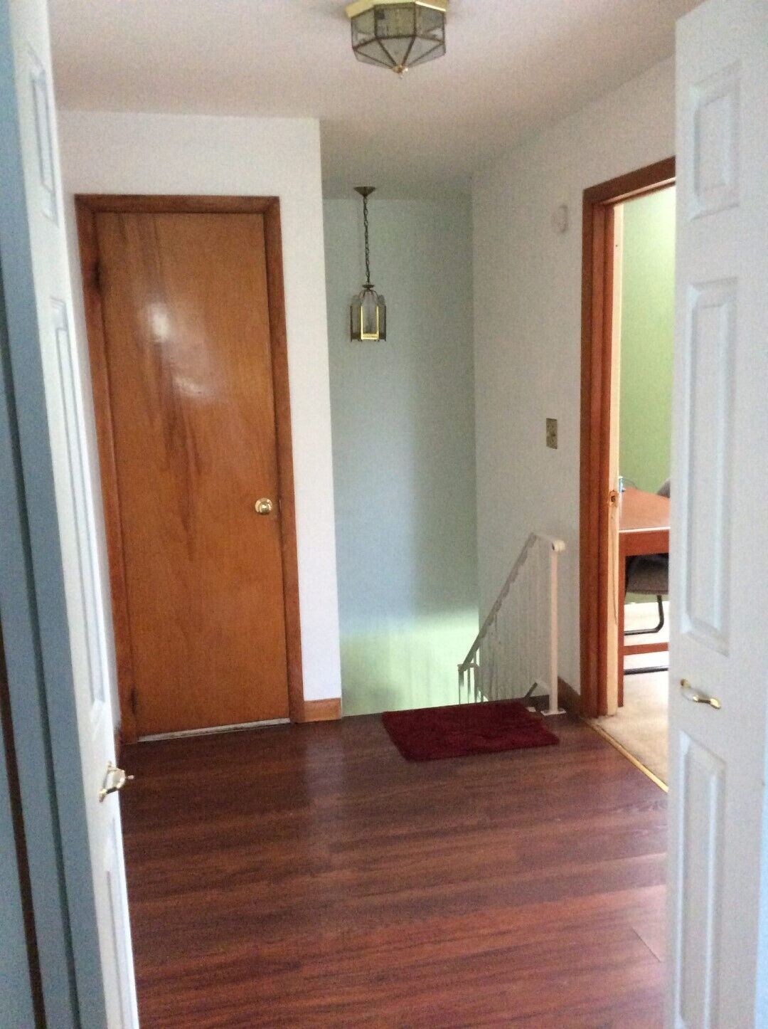 Een gang met houten vloer, een rood tapijt, een houten deur en een lamp.