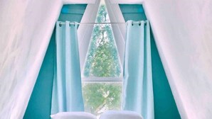 Un llit en una habitació amb forma de tenda i vista als arbres per la finestra.