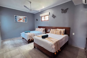A bedroom with two beds, a ceiling fan, a window with blinds, and butterfly wall art.