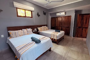 A bedroom with two beds, a ceiling fan, a window with blinds, and a wardrobe.