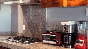 Een keuken met een gasfornuis, een heteluchtoven, een koffiezetapparaat en een blender.