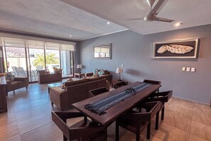 A spacious living area with a dining table, sofas, and a large window.