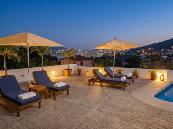 A rooftop terrace with lounge chairs, umbrellas, and a pool.