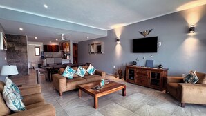 Een ruime woonkamer met een zithoek, een salontafel en een aan de muur bevestigde televisie.