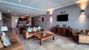 A spacious living room with a sofa set, a coffee table, and a television mounted on the wall.