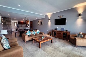 A spacious living room with a sofa set, a coffee table, and a television mounted on the wall.