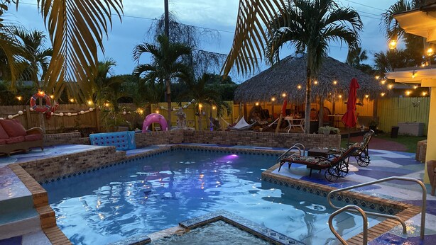 A swimming pool with a tiled deck, lounge chairs, and a thatched-roof structure.