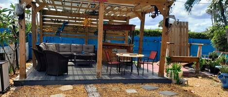 A covered outdoor patio with a wooden pergola, a sofa, a dining table, and chairs.