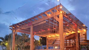 A wooden gazebo with a covered seating area, string lights, and a sign that reads "Cabaña."