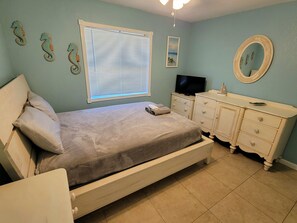 Quarto com cama, cômoda, televisão e arte decorativa de cavalos-marinhos na parede.