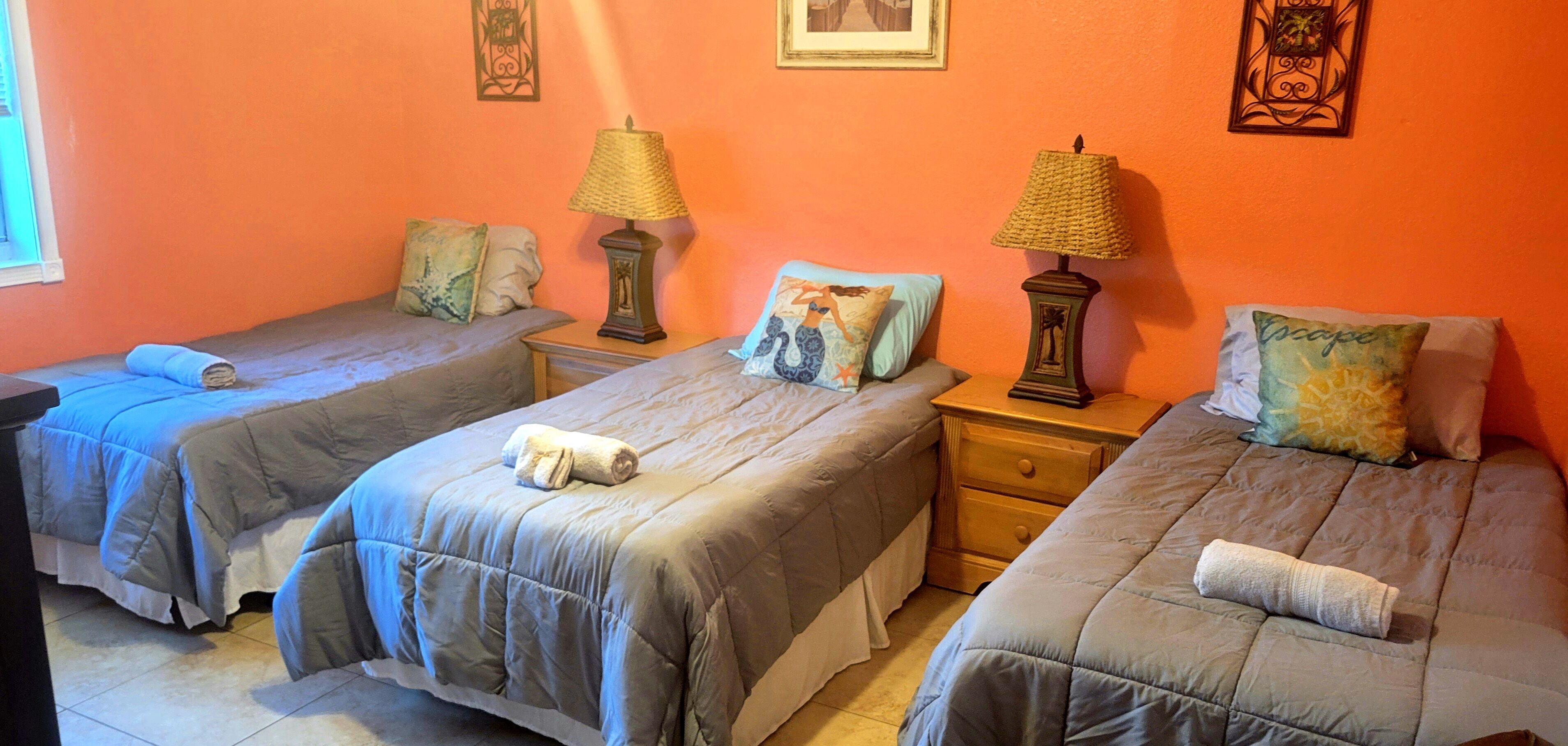 Une chambre dotée de trois lits, chacun agrémenté d’une serviette roulée, de deux tables de chevet avec des lampes et d’œuvres d’art décoratives murales.