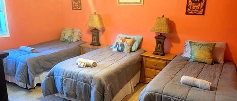 Une chambre dotée de trois lits, chacun agrémenté d’une serviette roulée, de deux tables de chevet avec des lampes et d’œuvres d’art décoratives murales.