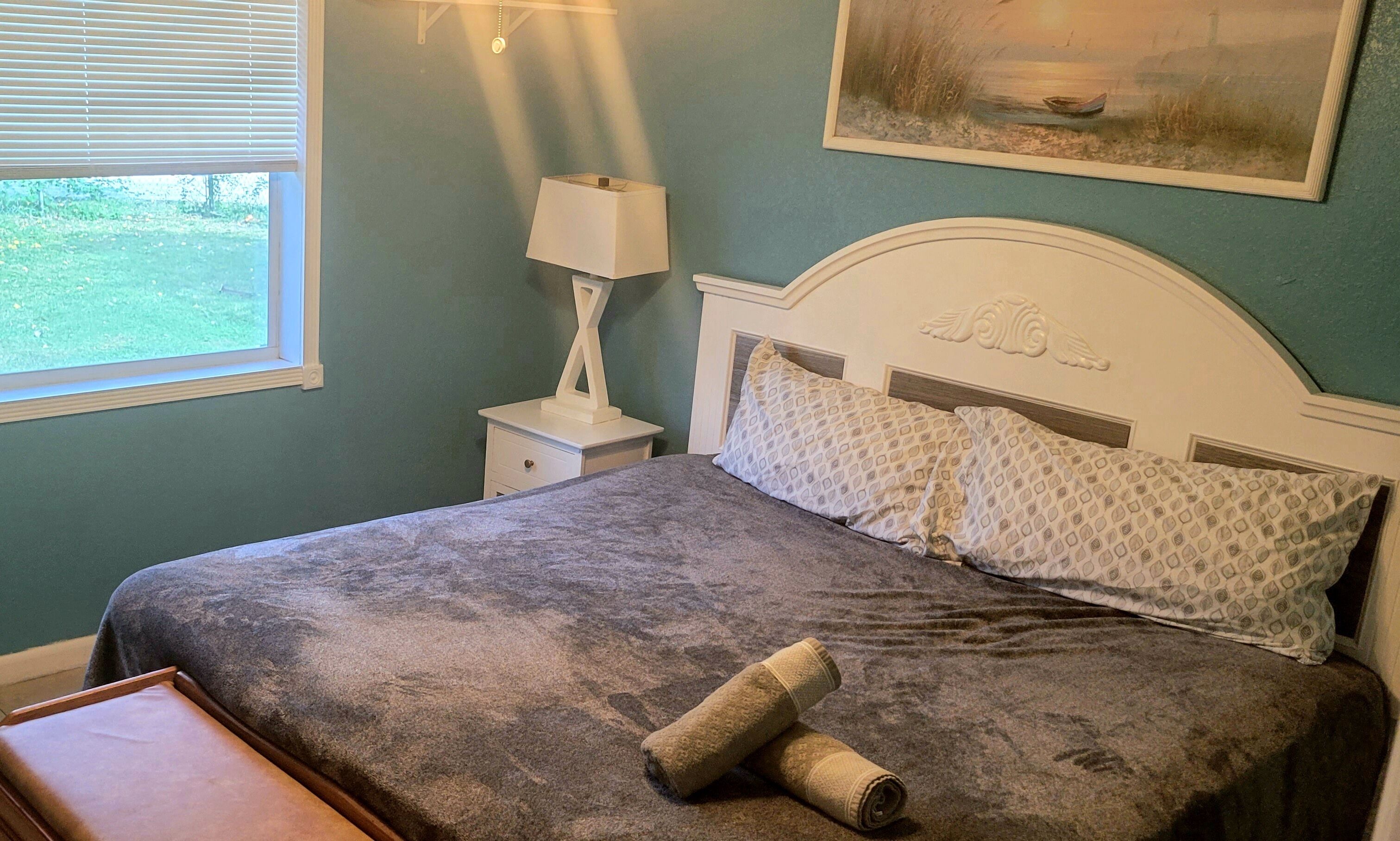 A bedroom with a bed, a nightstand, a lamp, and a painting on the wall.